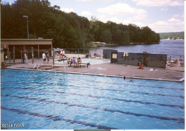 pool featuring a patio, a water view, and fence