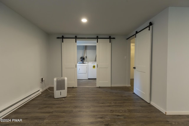 empty room featuring dark hardwood / wood-style floors, washing machine and clothes dryer, a barn door, and a baseboard heating unit