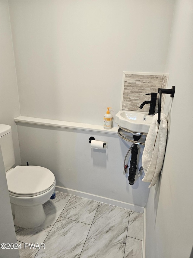 half bathroom with marble finish floor, toilet, and baseboards