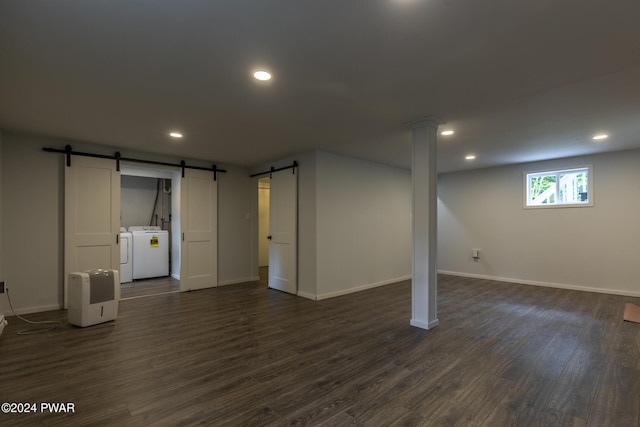 basement with a barn door, washing machine and clothes dryer, and dark hardwood / wood-style flooring