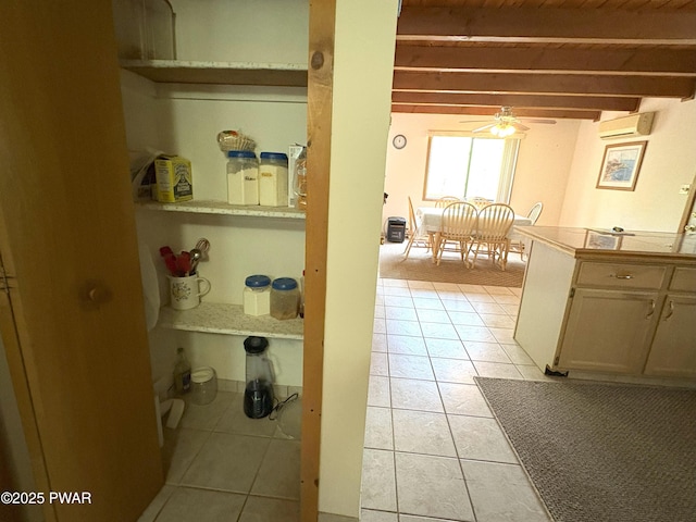 kitchen with a ceiling fan, light tile patterned floors, a wall unit AC, beamed ceiling, and tile counters