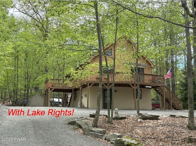 view of front of property with stairway, a wooden deck, stucco siding, and a forest view