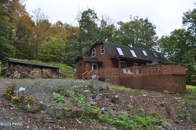 rear view of house with a shingled roof, faux log siding, a wooden deck, and a gambrel roof