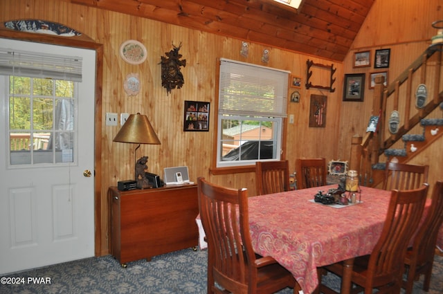 carpeted dining room featuring lofted ceiling, wooden walls, and stairway