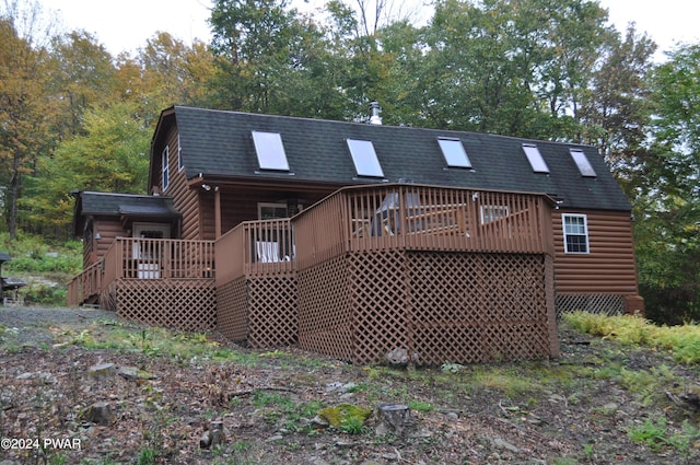 back of house with roof with shingles, log veneer siding, a wooden deck, and a gambrel roof