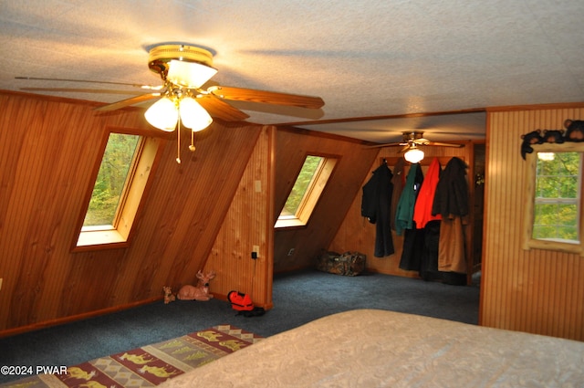 unfurnished bedroom with a skylight, carpet flooring, a ceiling fan, and wooden walls