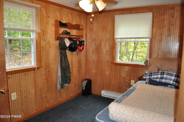 bedroom with wooden walls, multiple windows, baseboard heating, and carpet flooring