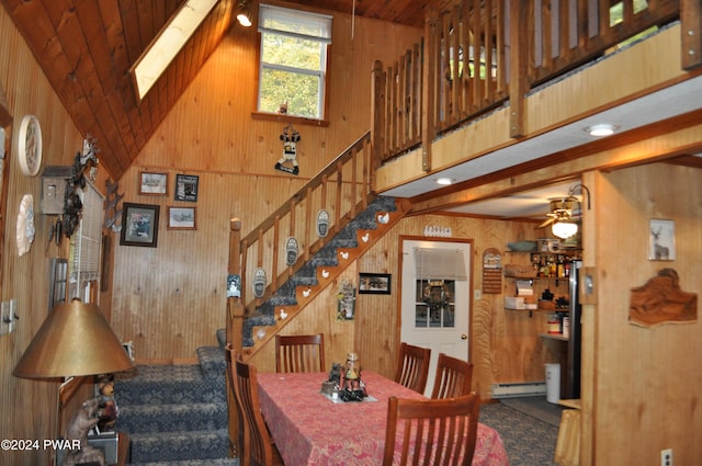 carpeted dining room with high vaulted ceiling, stairway, a baseboard radiator, and wooden walls