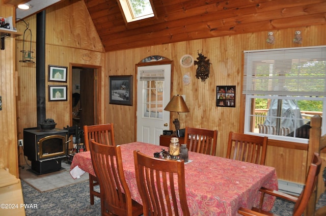 dining area featuring vaulted ceiling with skylight, wood walls, and a wood stove