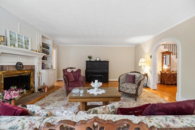 living area featuring arched walkways, a fireplace, wood finished floors, baseboards, and ornamental molding