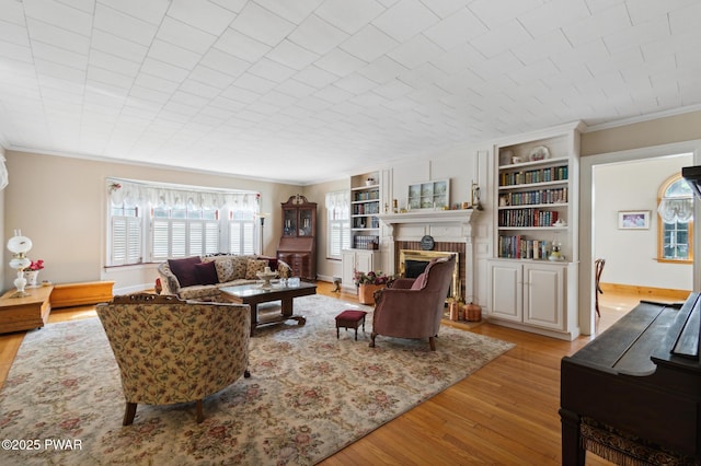 living area featuring crown molding, a brick fireplace, wood finished floors, and built in shelves