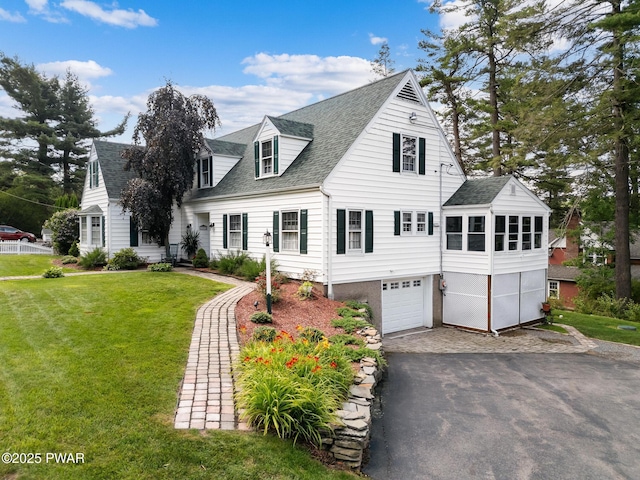 new england style home with a garage, aphalt driveway, roof with shingles, and a front yard