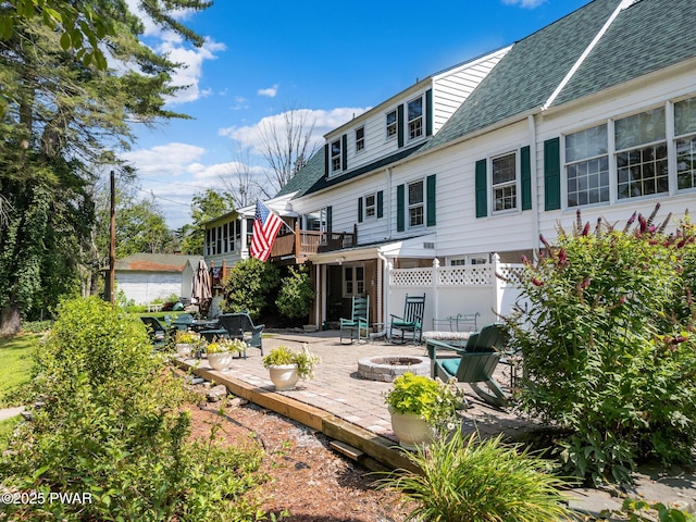 rear view of property with a patio, a fire pit, roof with shingles, and a wooden deck