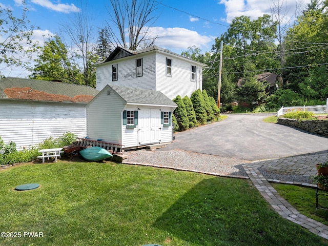 rear view of property featuring a lawn, an outbuilding, roof with shingles, and a storage shed