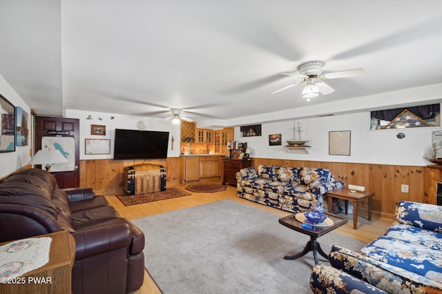 living room featuring wood walls, a wainscoted wall, a ceiling fan, and light wood finished floors