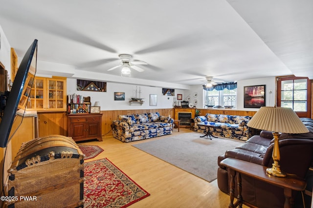 living area with wooden walls, a wainscoted wall, a ceiling fan, and wood finished floors