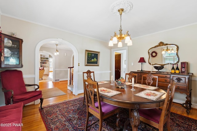 dining room with visible vents, crown molding, arched walkways, light wood finished floors, and an inviting chandelier