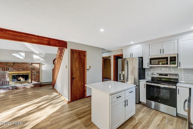 kitchen featuring backsplash, white cabinets, a brick fireplace, appliances with stainless steel finishes, and a kitchen island