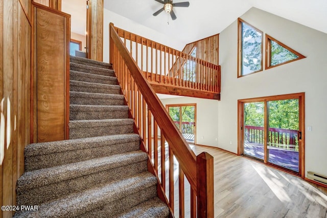 staircase with hardwood / wood-style floors, ceiling fan, a towering ceiling, and a baseboard heating unit