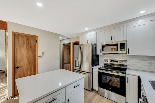 kitchen with decorative backsplash, appliances with stainless steel finishes, light wood-type flooring, a baseboard heating unit, and white cabinets