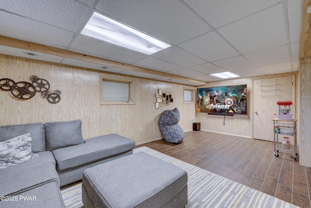 living room with hardwood / wood-style floors, a drop ceiling, and wood walls