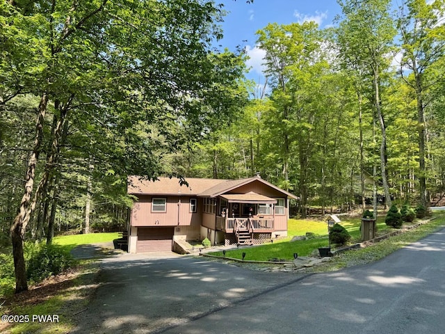 130 Grasshopper Ln, Greentown, PA 18426 - view of front of house with asphalt driveway, an attached garage, a view of trees, a wooden deck, and a shingled roof