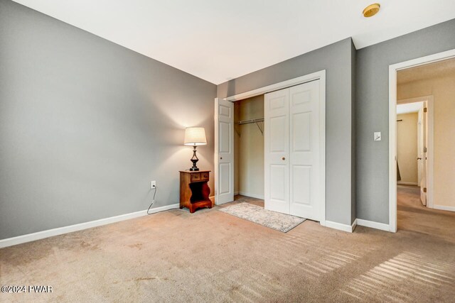 unfurnished bedroom with light colored carpet and a closet