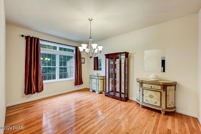 unfurnished dining area with wood-type flooring and a notable chandelier