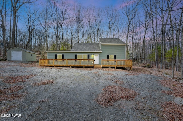 view of front of home with an outdoor structure, roof with shingles, a deck, and a storage shed