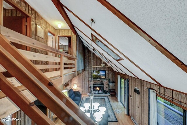24 Lakewood Dr, Lake Ariel, PA 18436 - stairs with wooden walls, vaulted ceiling, a lit fireplace, wood finished floors, and a chandelier