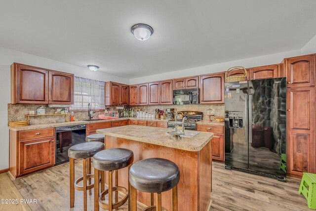 2106 Blueberry Ct, Bushkill, PA 18324 - kitchen with black appliances, light wood finished floors, light countertops, a breakfast bar area, and an island with sink