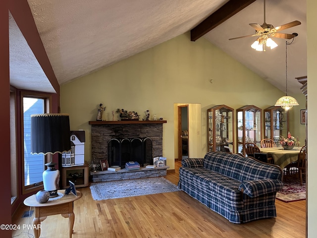 living room featuring a wealth of natural light, a textured ceiling, beam ceiling, hardwood / wood-style floors, and a stone fireplace