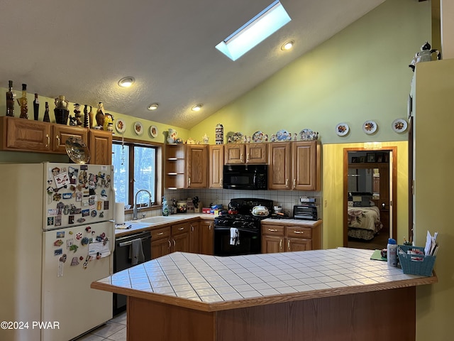 kitchen featuring tile countertops, backsplash, black appliances, sink, and a skylight