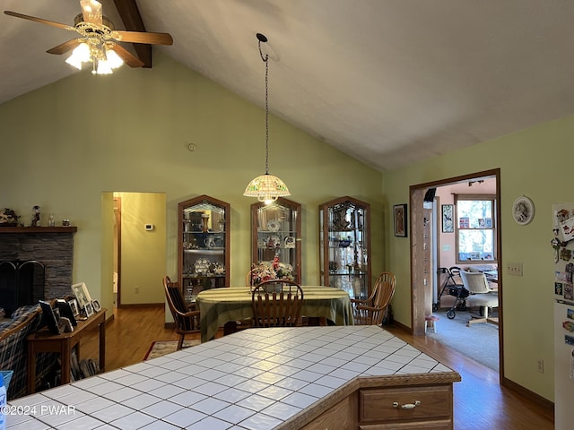 dining area featuring hardwood / wood-style flooring, vaulted ceiling with beams, ceiling fan, and a fireplace