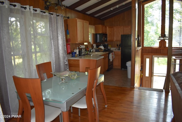 dining room featuring light wood-type flooring, lofted ceiling with beams, wooden walls, and sink