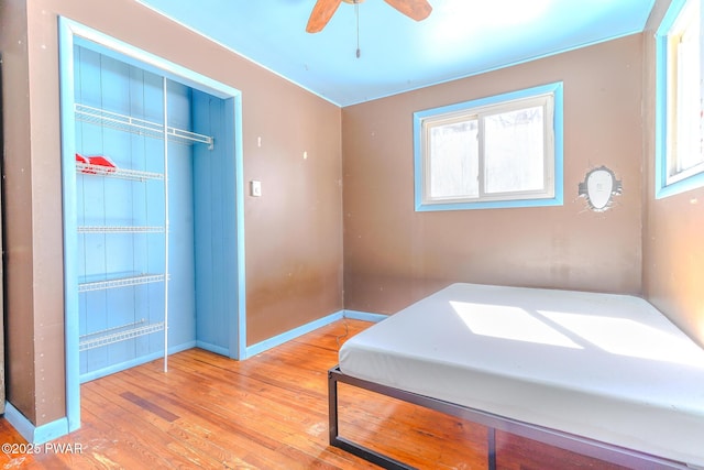 bedroom featuring a ceiling fan, a closet, baseboards, and wood finished floors