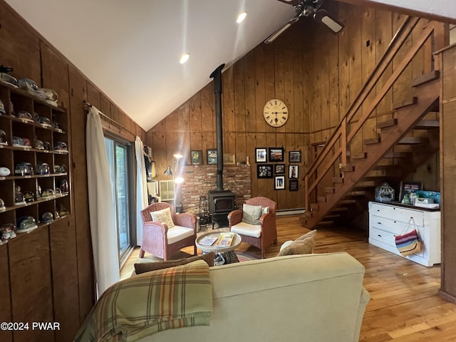 living room featuring a wood stove, ceiling fan, wooden walls, and vaulted ceiling