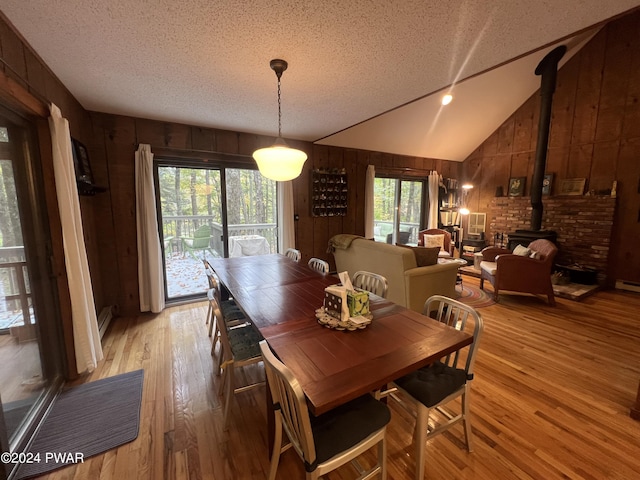 dining area featuring lofted ceiling, a healthy amount of sunlight, a textured ceiling, and a wood stove