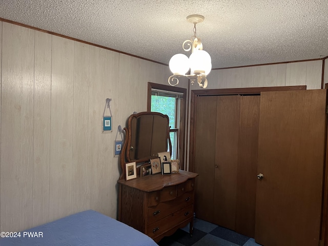 bedroom with a closet, wood walls, an inviting chandelier, and a textured ceiling