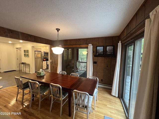 dining area with a textured ceiling, baseboard heating, light wood-type flooring, and wooden walls