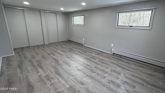 unfurnished bedroom featuring light wood-type flooring, multiple windows, and a baseboard heating unit