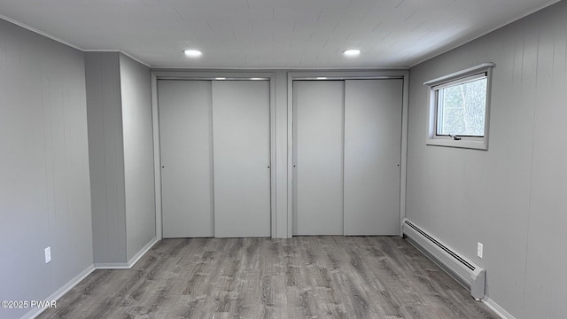 unfurnished bedroom featuring two closets, baseboard heating, and light hardwood / wood-style floors