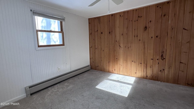 carpeted spare room with ceiling fan, wood walls, and a baseboard heating unit