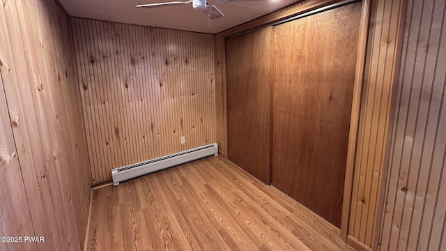 empty room featuring light hardwood / wood-style flooring, a baseboard heating unit, and wood walls