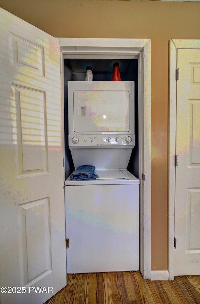 laundry room with wood finished floors, stacked washing maching and dryer, and laundry area