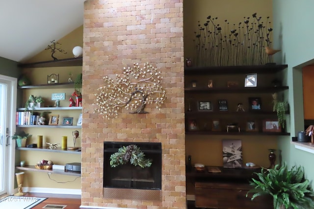 living area with built in features, vaulted ceiling, visible vents, and a fireplace