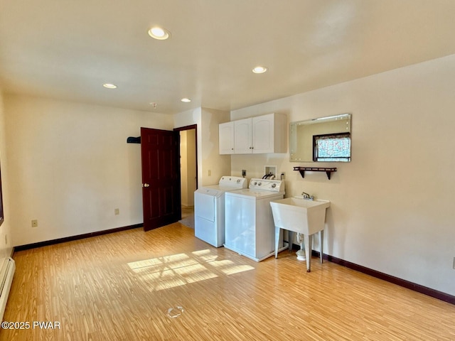 clothes washing area featuring sink, a baseboard heating unit, cabinets, light hardwood / wood-style floors, and washer and dryer