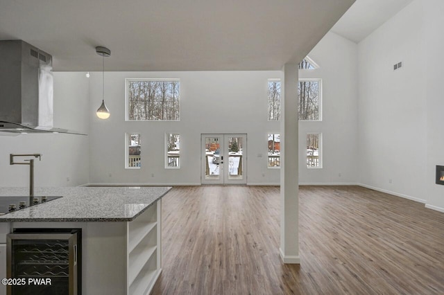 unfurnished living room with a high ceiling, wine cooler, light hardwood / wood-style floors, and french doors