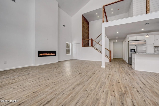 unfurnished living room featuring high vaulted ceiling and light hardwood / wood-style flooring