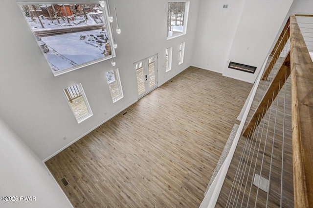 foyer entrance featuring a towering ceiling, wood finished floors, a glass covered fireplace, and baseboards
